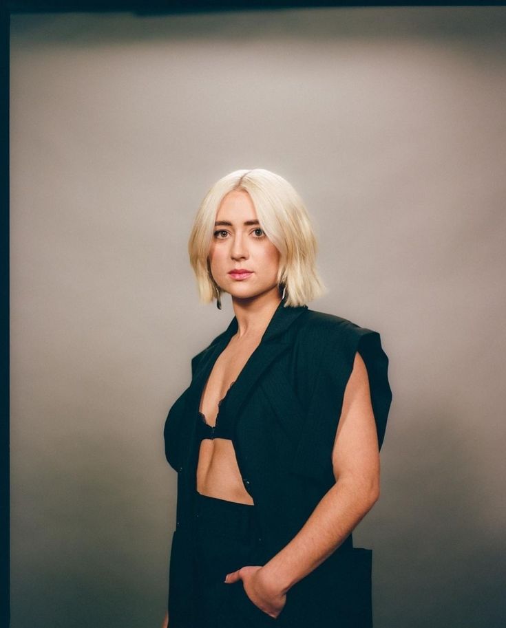 a woman with blonde hair wearing a black dress and posing for a photo in front of a gray background