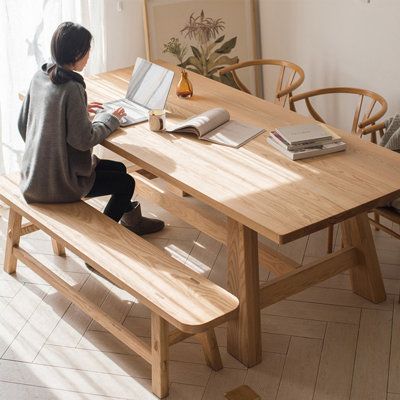 a woman sitting at a wooden table with a laptop computer on top of her lap