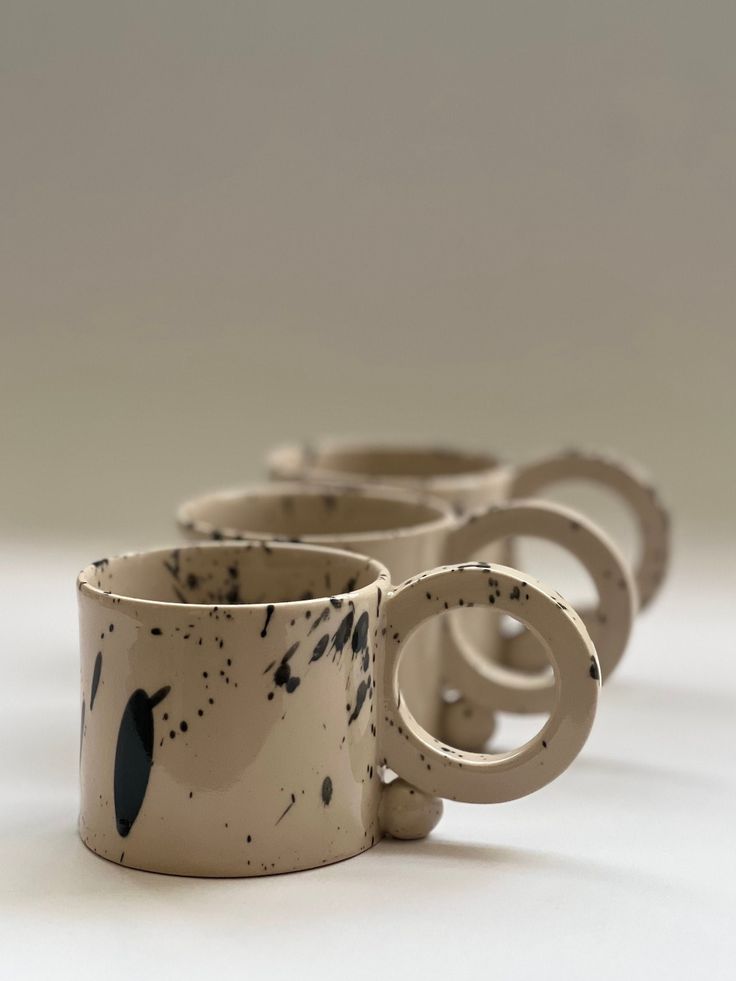 four coffee mugs are lined up in a row on a white surface with black spots