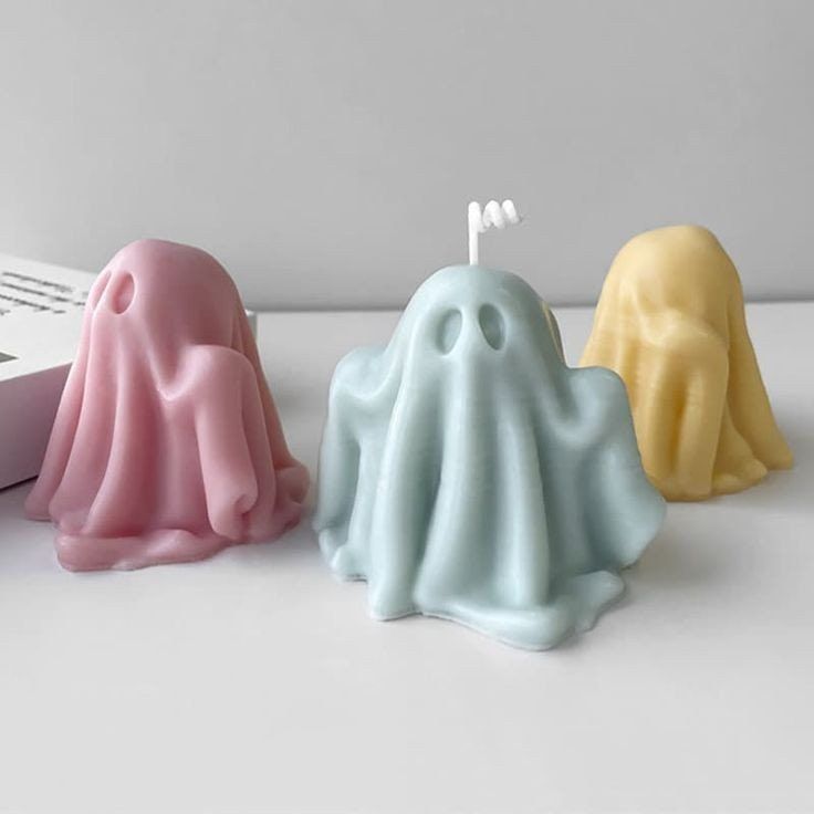 three candles in the shape of ghost sitting next to each other on a white surface