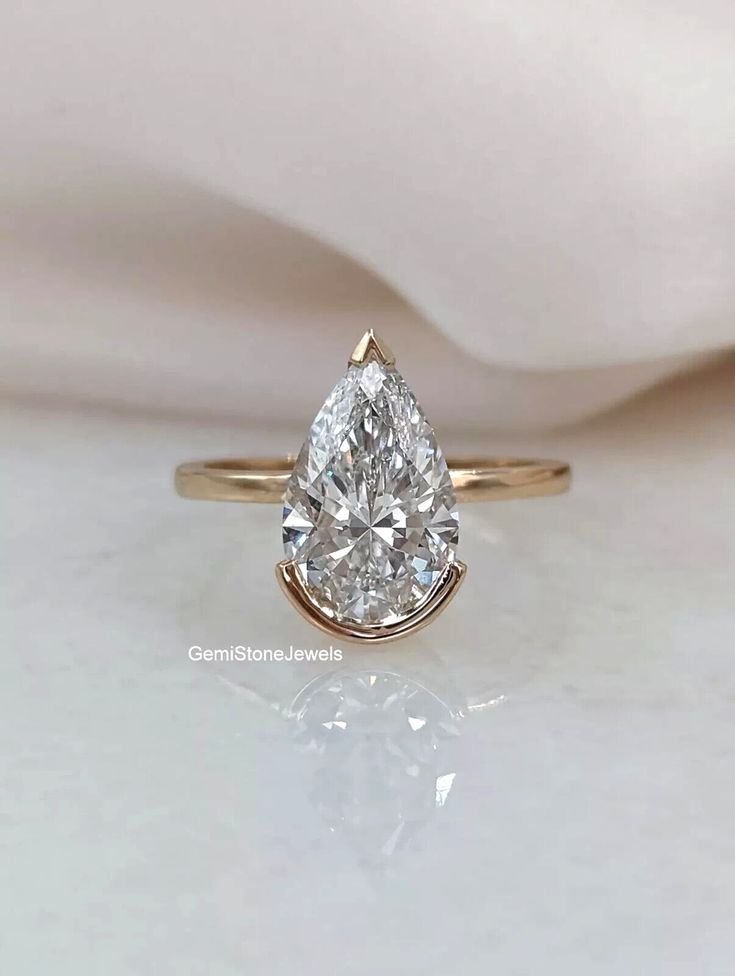 a pear shaped diamond engagement ring sitting on top of a white cloth