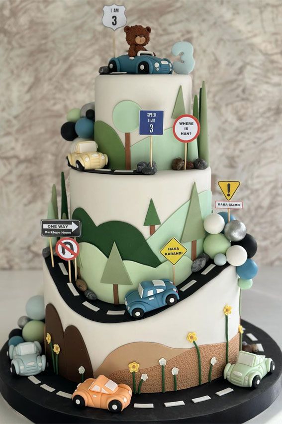 a three tiered cake with cars and trees on it's sides is decorated in pastel colors