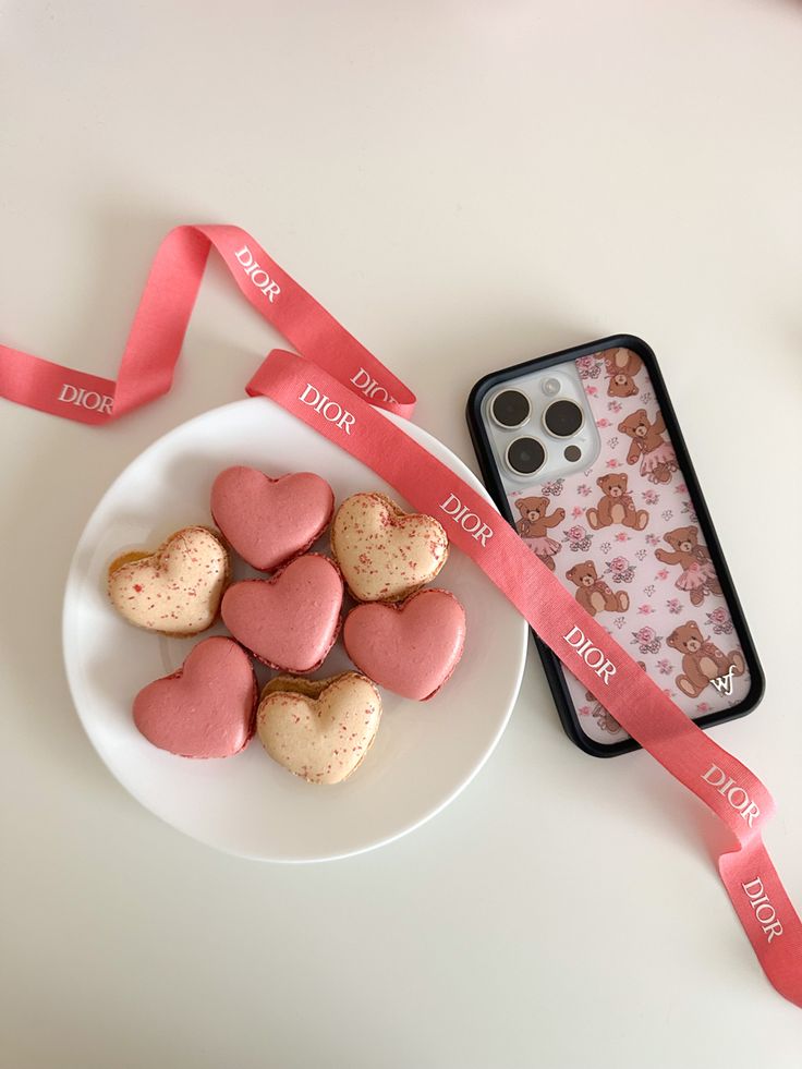 some heart shaped cookies are on a plate next to a pink ribbon and cell phone