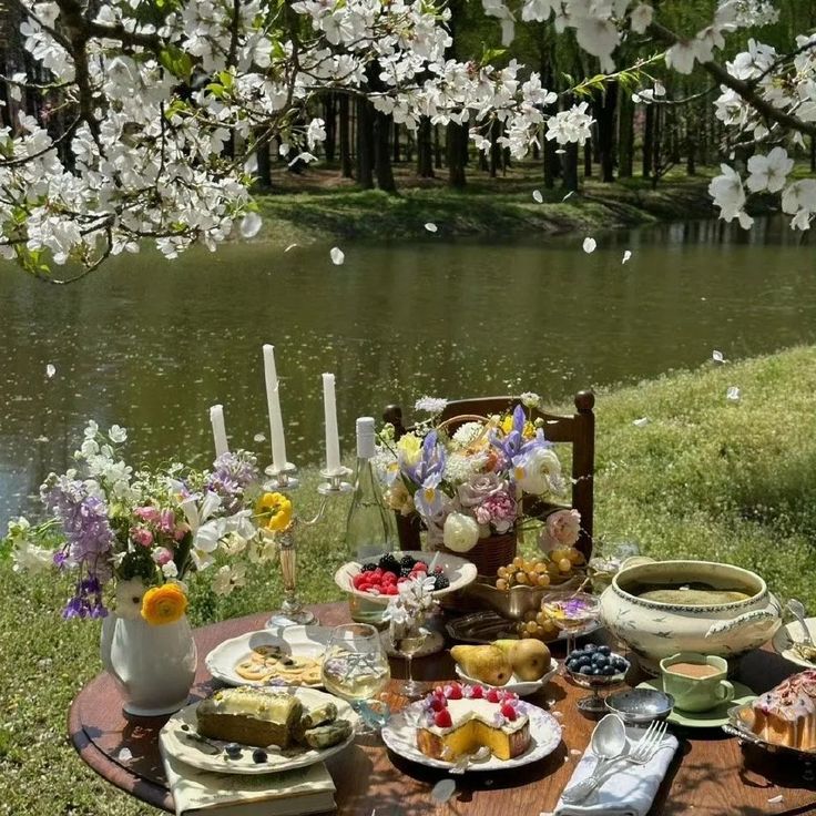 a picnic table set up with food and flowers by the water in front of it