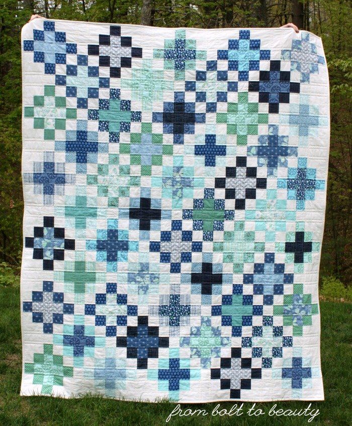 a blue and green quilt hanging from a clothes line in the grass with trees in the background