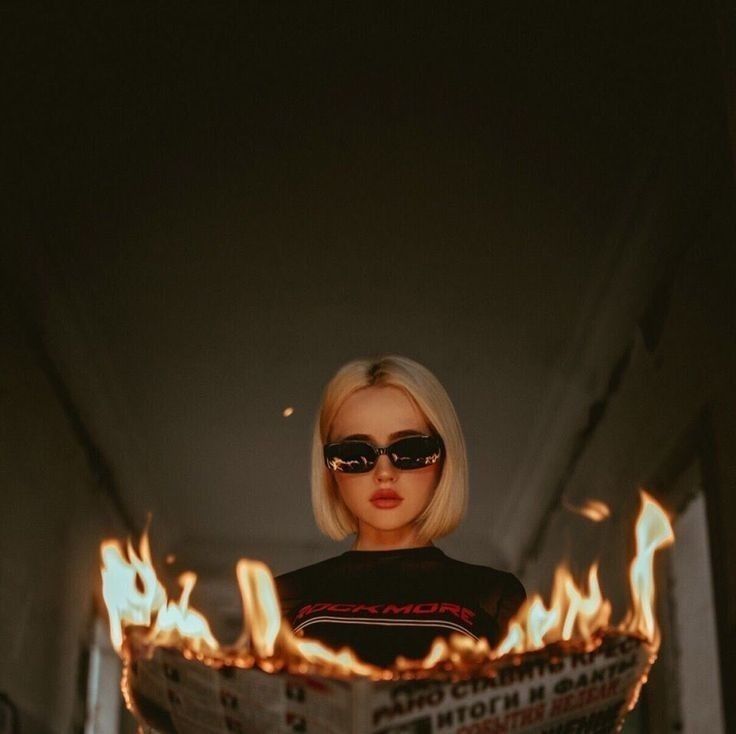 a barbie doll wearing sunglasses and holding a newspaper with flames in front of her face