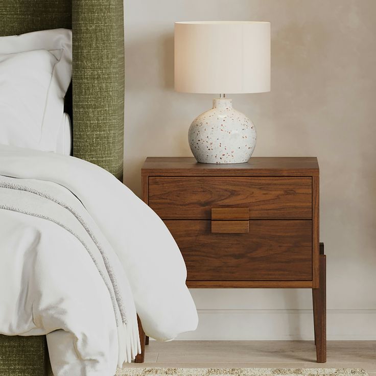 a nightstand with a lamp on it next to a bed