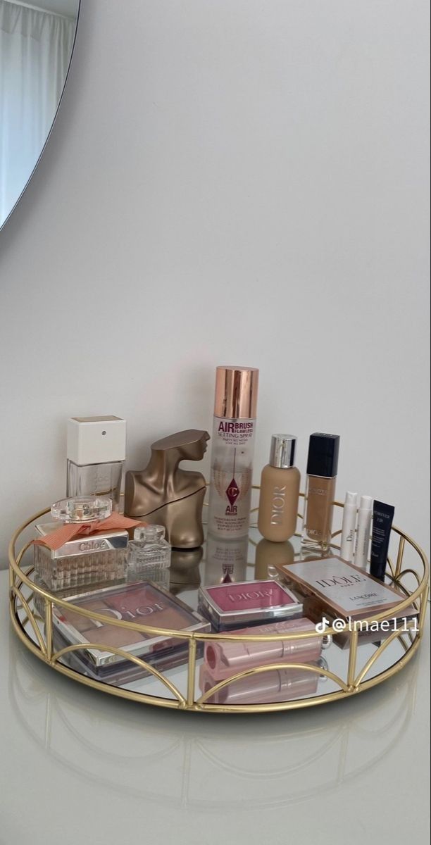 a round gold tray with cosmetics and perfumes on the counter in front of a mirror