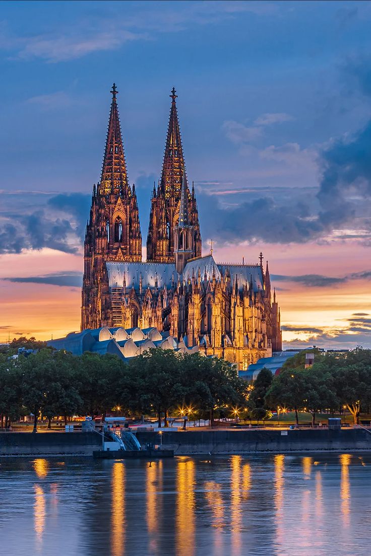 the cathedral is lit up at night by the water's edge with boats in front