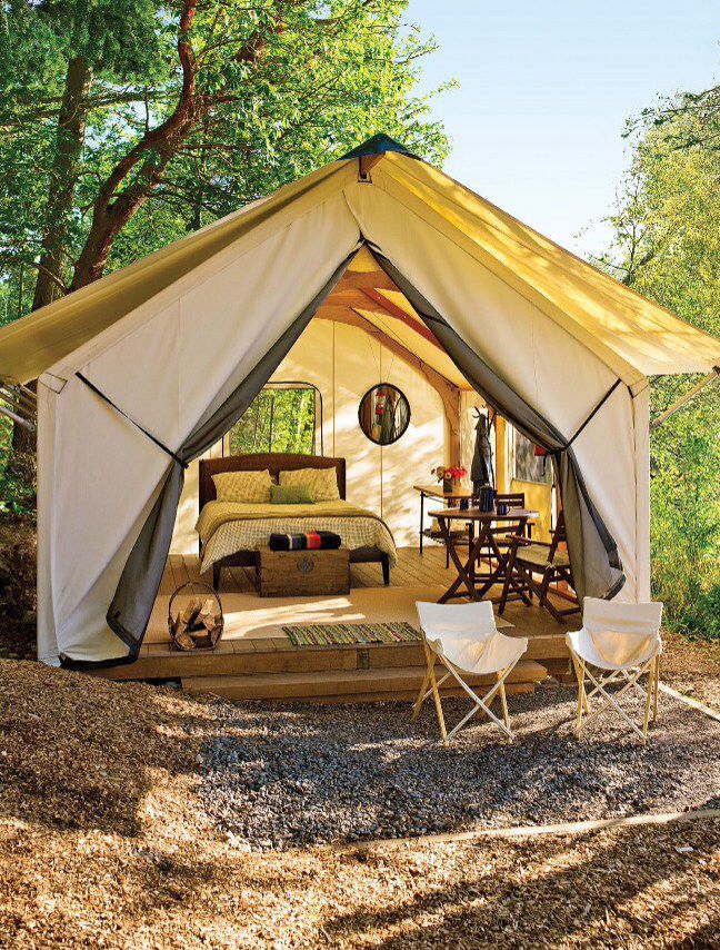 a tent is set up in the woods with two chairs and a bed inside it