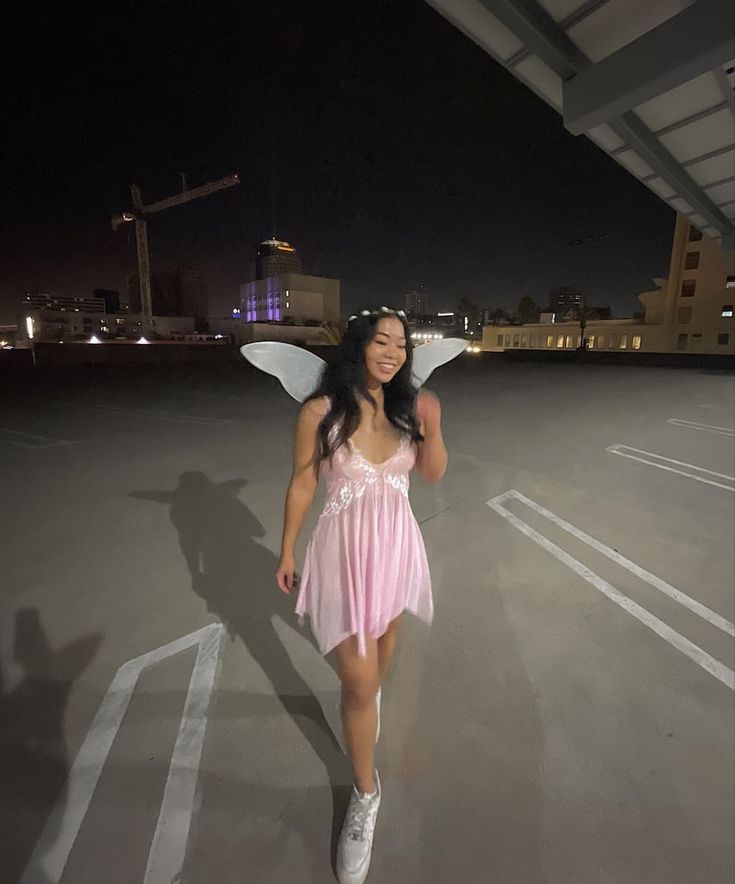 a woman in a pink dress and fairy wings is walking through an empty parking lot