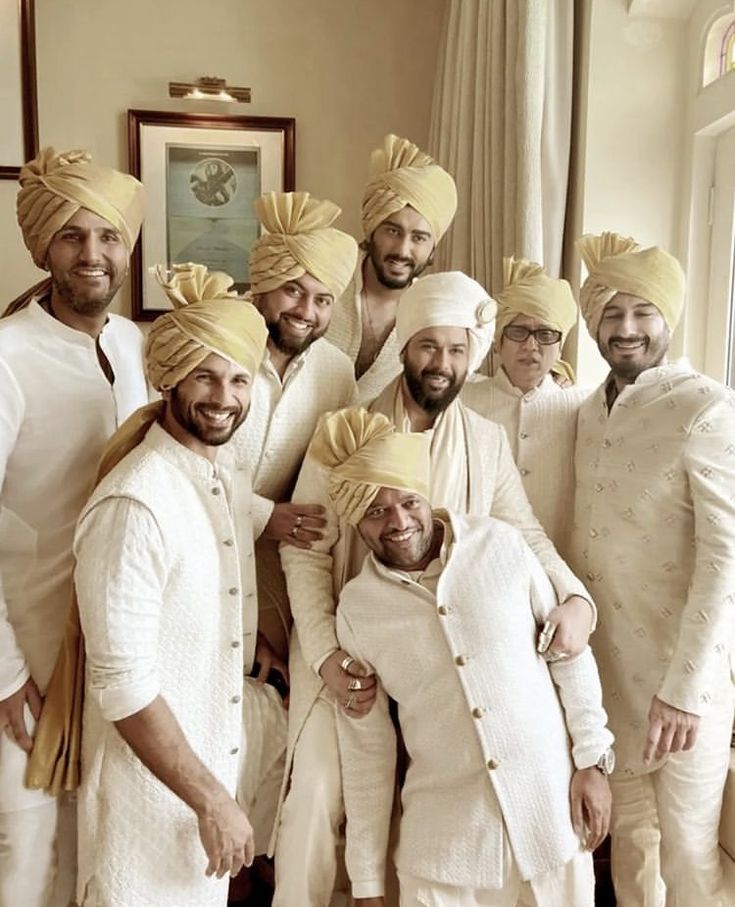 a group of men standing next to each other in front of a window wearing turbans