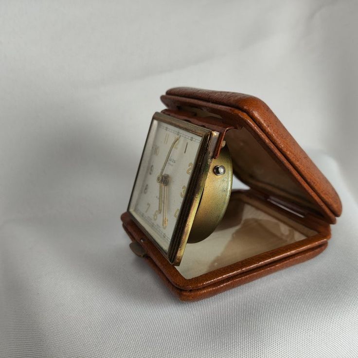 an old pocket watch is sitting on a white cloth covered surface with its reflection in the mirror