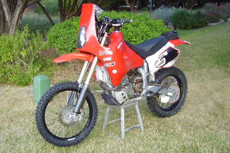 a red dirt bike parked on top of a grass covered field next to a bush