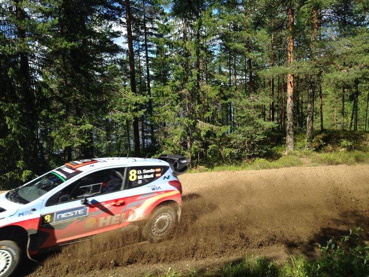 a rally car driving on a dirt road in the woods