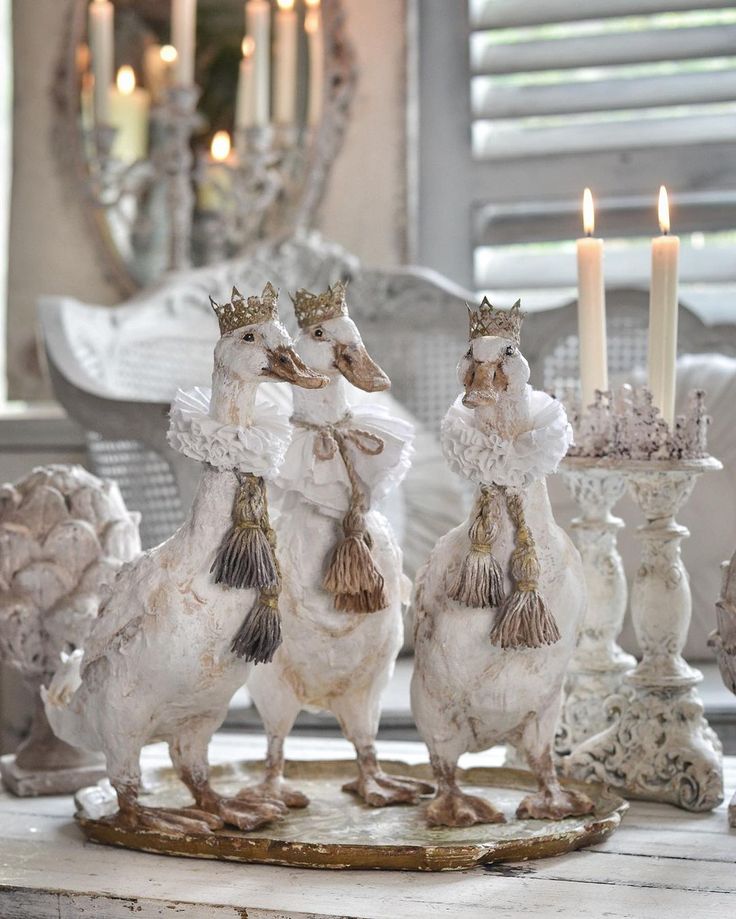 three white rooster figurines sitting on top of a wooden table next to candles