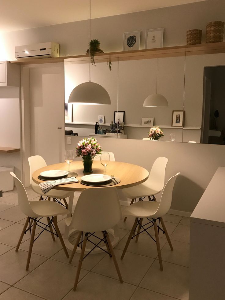 a dining table with white chairs and flowers on it in the middle of a kitchen