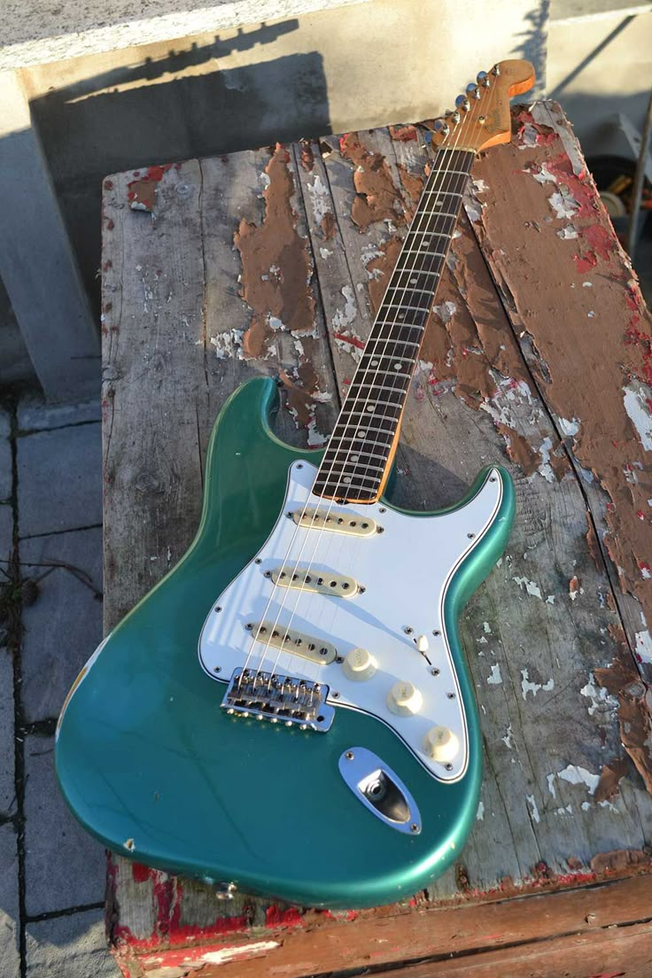 a green electric guitar sitting on top of a wooden pallet next to a brick wall