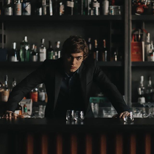 a man sitting at a bar with lots of bottles behind him