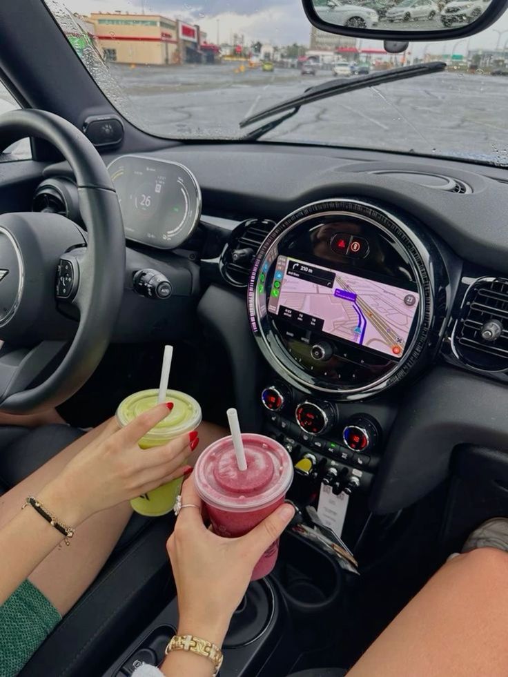 a woman sitting in the driver's seat of a car holding a drink