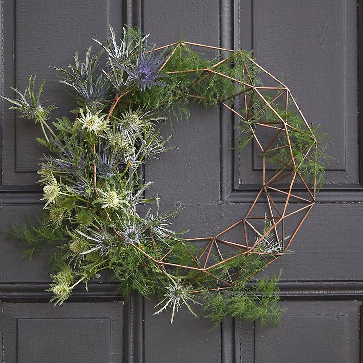 a wreath made out of branches and flowers hanging on a gray painted door with metal bars