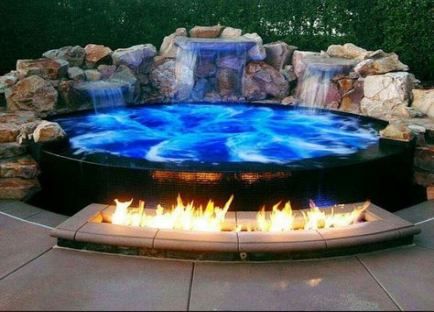 an outdoor fire pit with blue water and rocks around it, on a patio surrounded by greenery