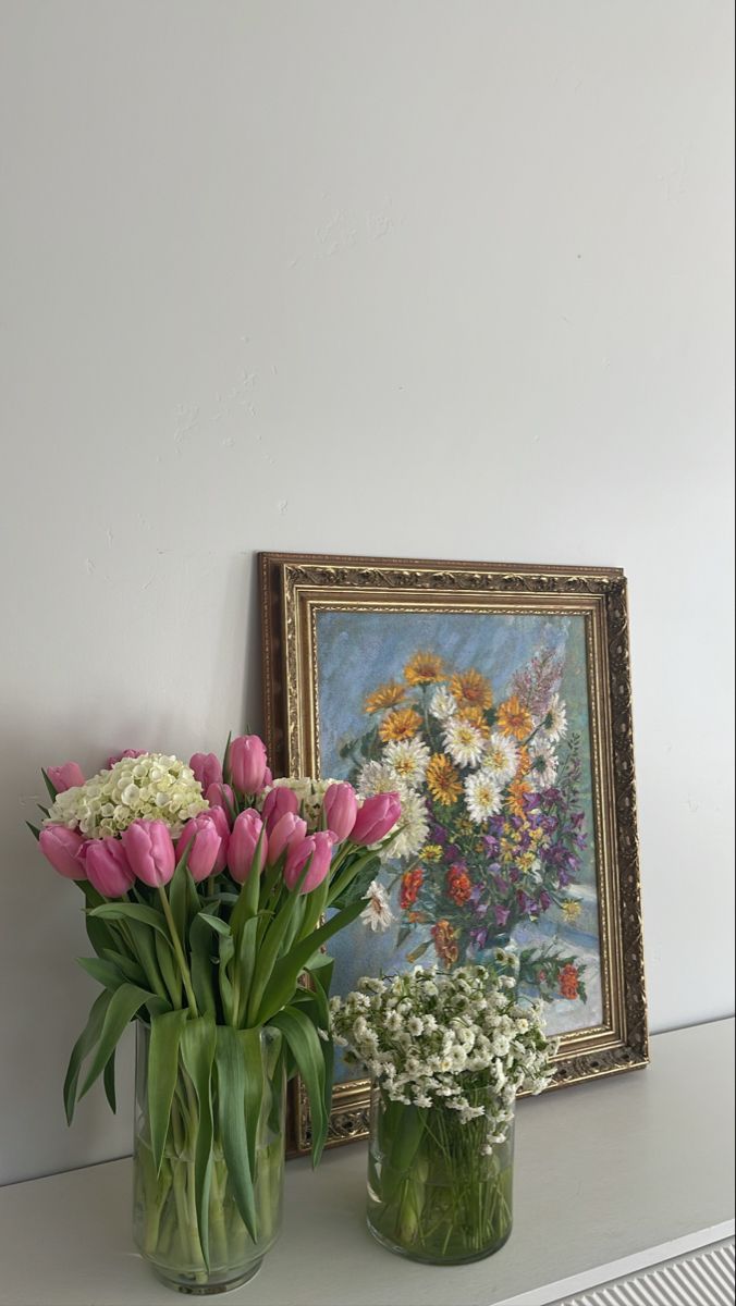 two vases filled with flowers sit on a shelf next to a painting and framed artwork