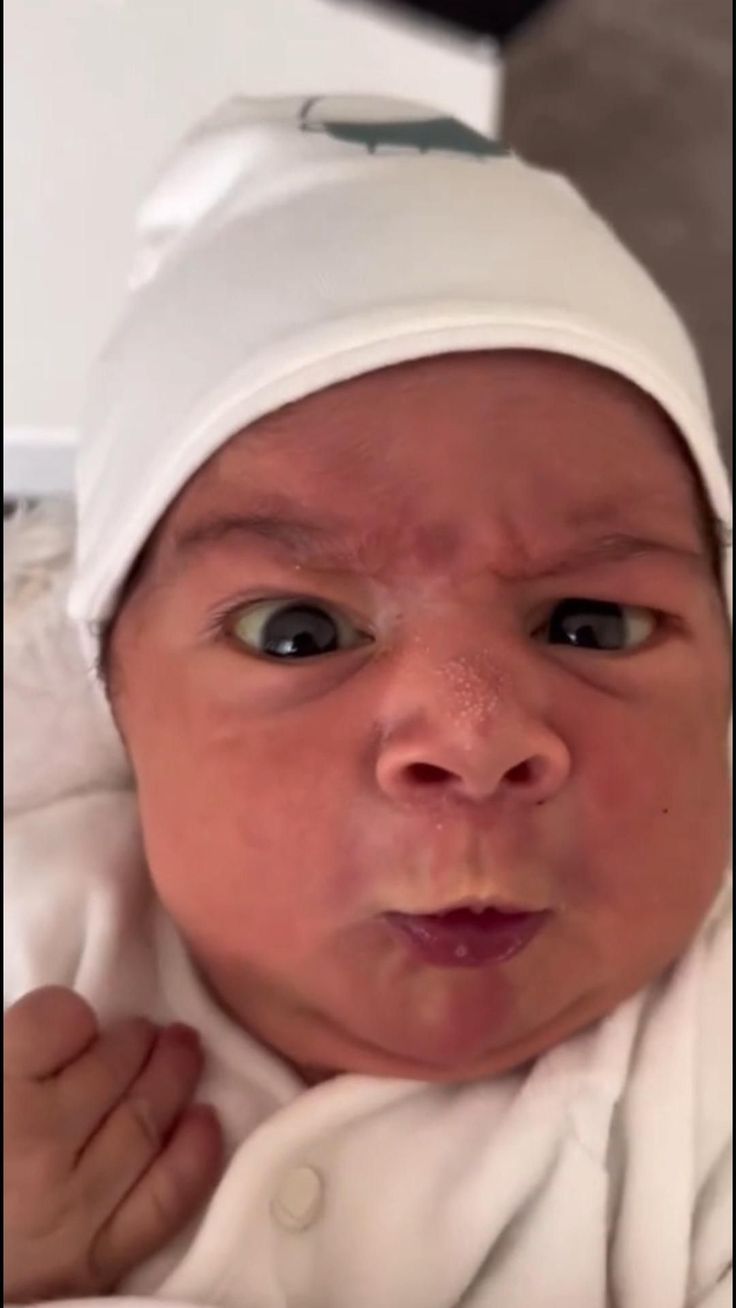 a close up of a baby wearing a white hat and looking at the camera with an angry look on its face