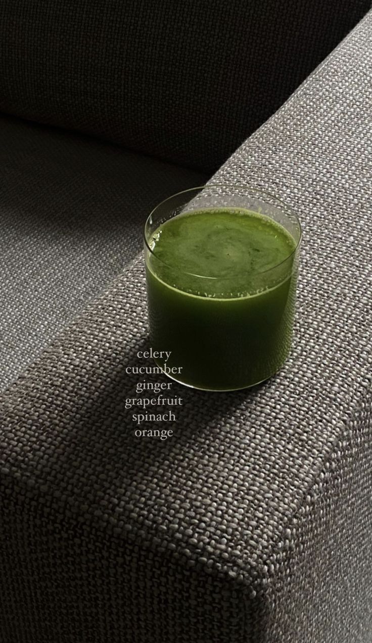 a glass filled with green liquid sitting on top of a couch