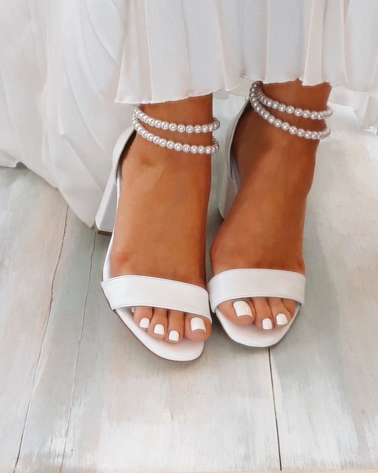 the bride's shoes are all white and have pearls on their ankle straps