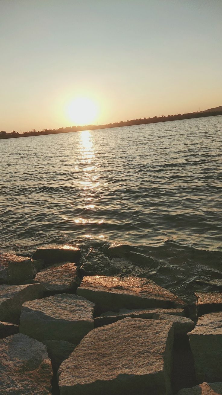 the sun is setting over the water and rocks