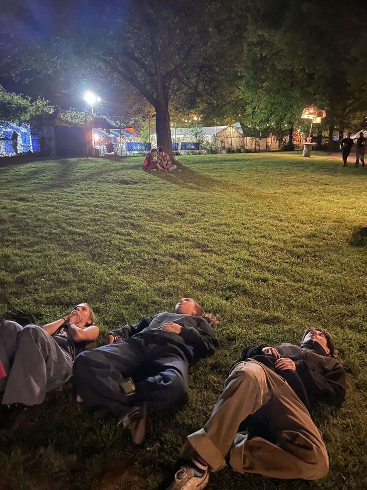 two men laying on the ground in front of a tree at night with their heads down