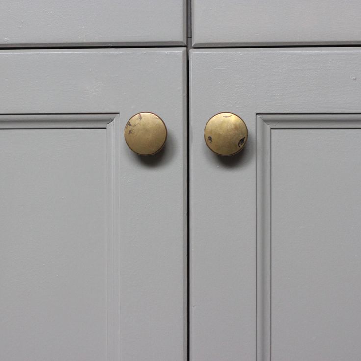 two gold knobs are on the front of a gray cabinet with white doors and drawers