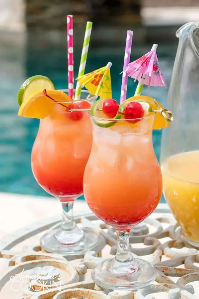 two glasses filled with drinks sitting on top of a table next to a swimming pool