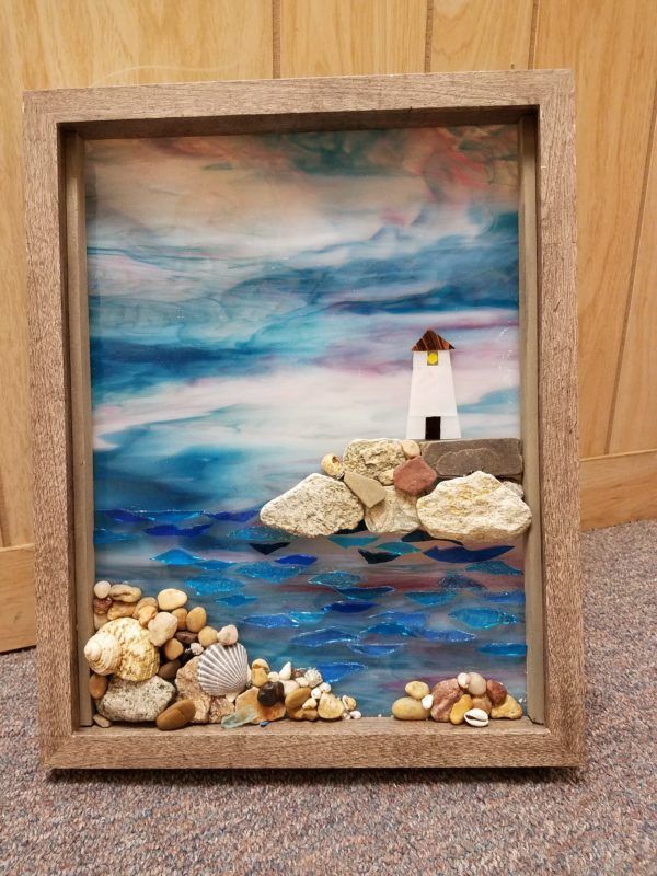 a painting with rocks, shells and a light house on the top is in a wooden frame