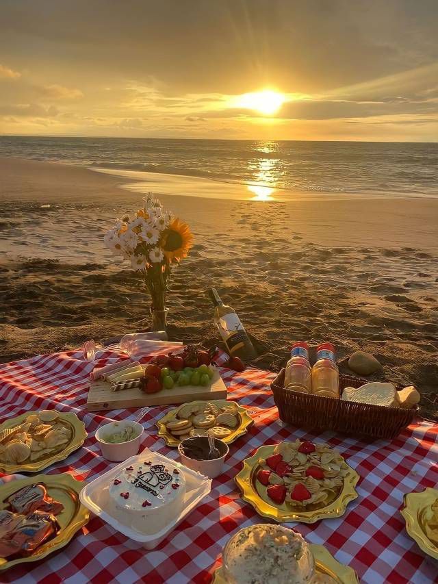 a picnic on the beach is set up with food and flowers in front of the ocean