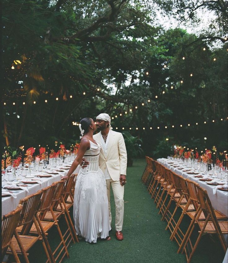 a bride and groom kissing in front of an outdoor dinner table set with white linens