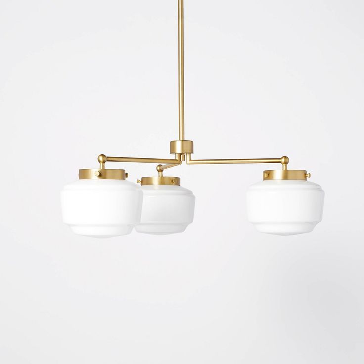 three white glass shades hang from a brass - plated chandelier in an empty room