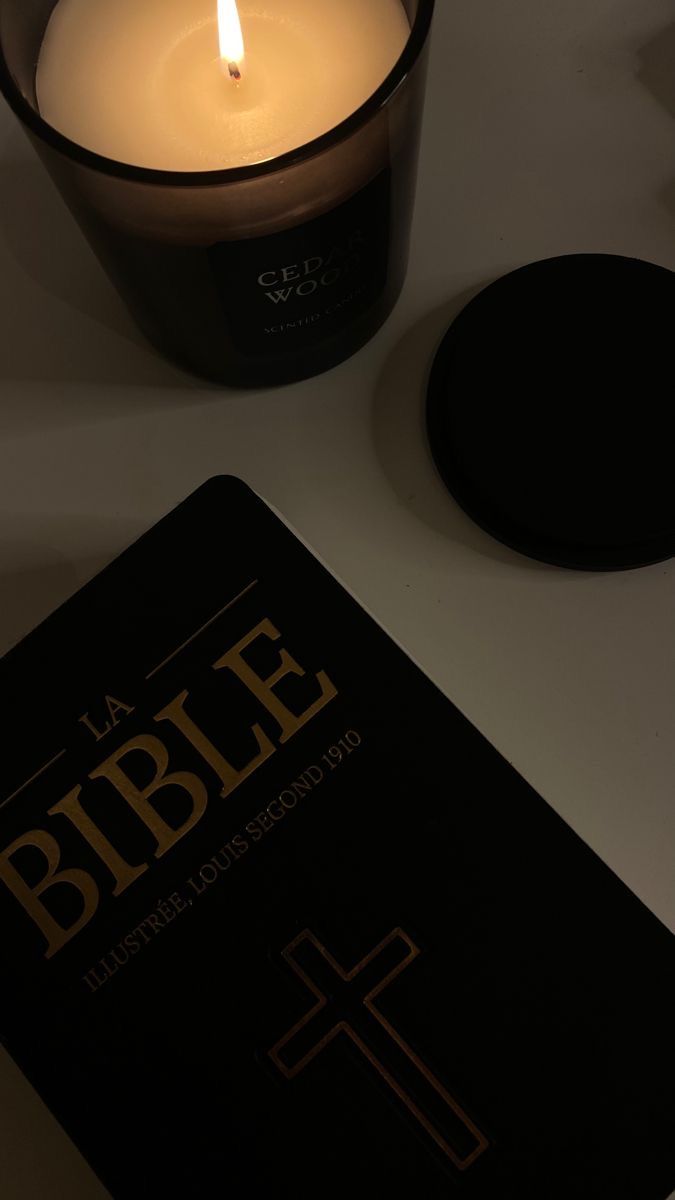 a bible next to a lit candle on a white table top with black coasters