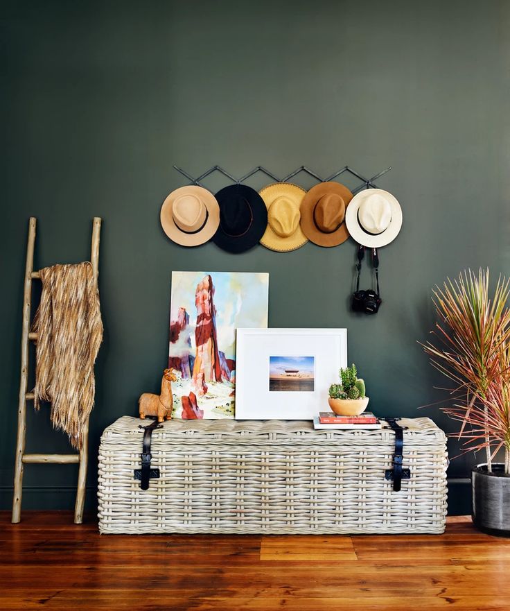 a wicker trunk with hats on top and pictures hanging above it in front of a green wall