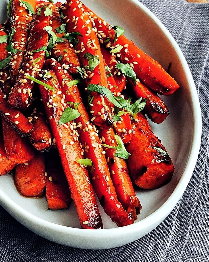 a white bowl filled with carrots covered in sesame seeds and garnishes