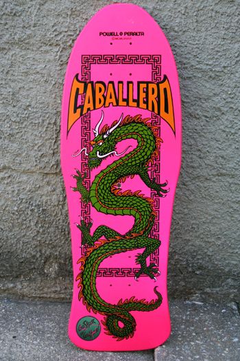 a pink skateboard with a green dragon on the front and yellow lettering that says caballierd