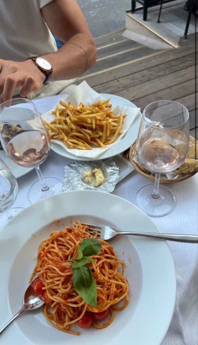 a plate of spaghetti with tomato sauce and parmesan cheese on the side next to wine glasses