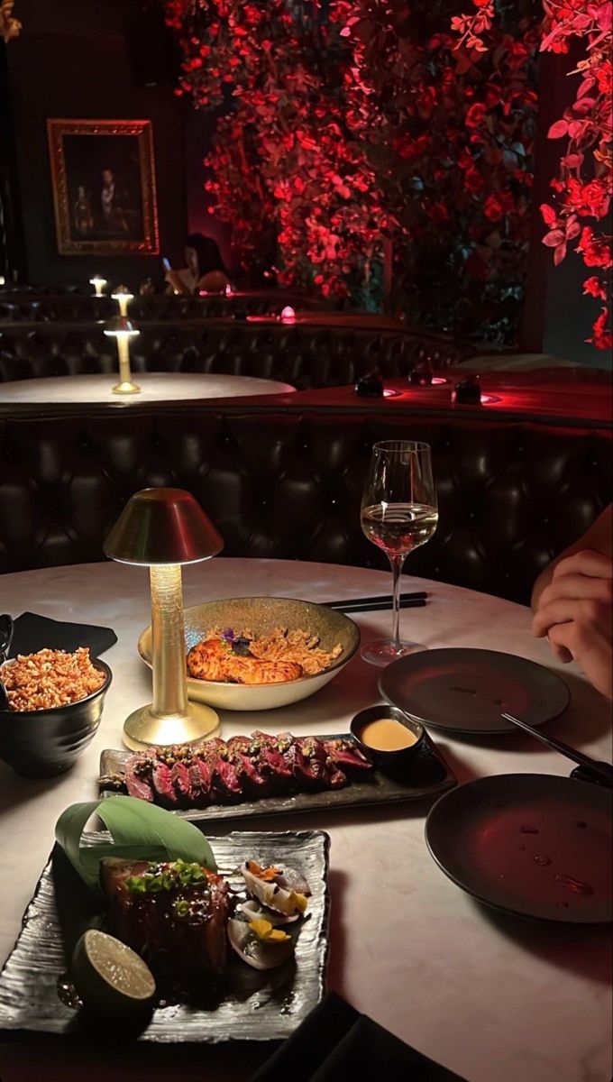 a table topped with lots of food next to a glass of wine and a lamp