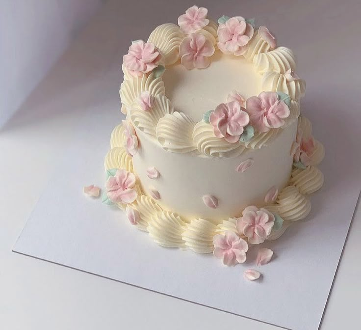 a white cake with pink and blue flowers on it's side sitting on top of a piece of paper