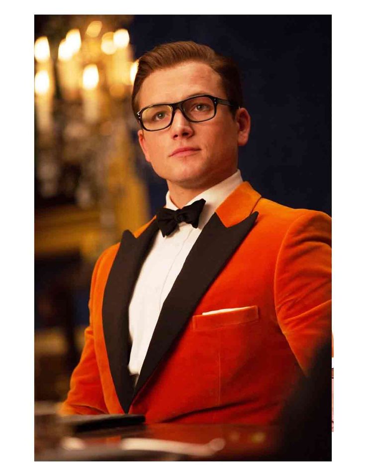 a man in an orange tuxedo and black bow tie sitting at a table