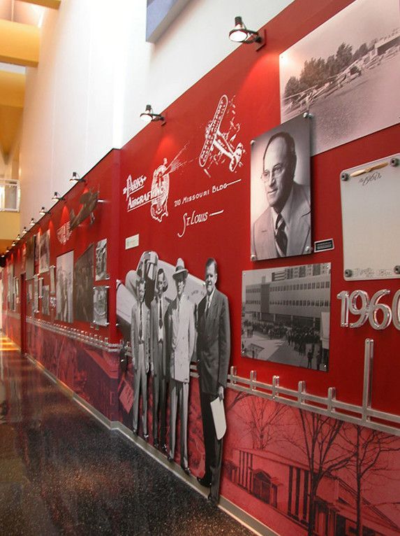 a red wall with many pictures on it and some people standing in front of it