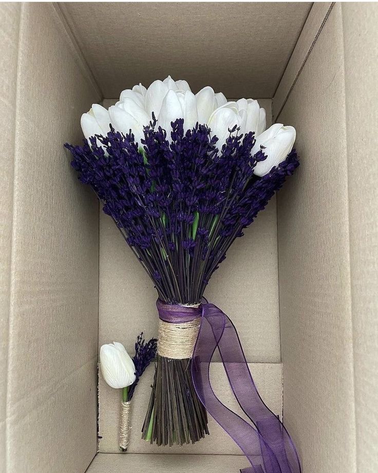 a bouquet of flowers in a box with purple ribbon and some white tulips