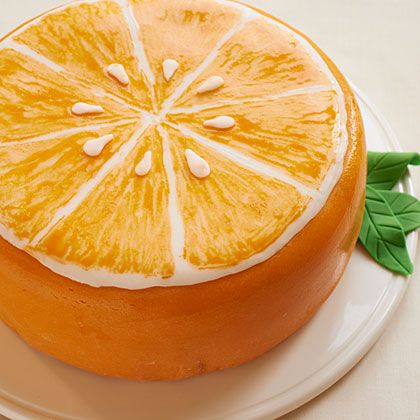 an orange cake with white frosting and green leaves on the top is sitting on a plate