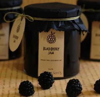 some blackberries are next to a jar of jam on a table with tags around it